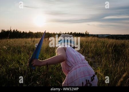 Fille jouant avec paper planes dans un pré au coucher du soleil en été Banque D'Images
