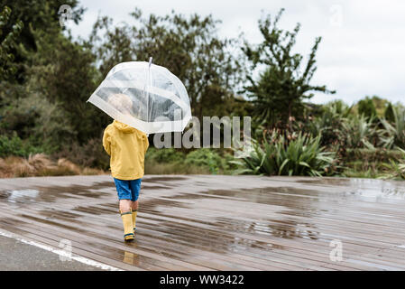 Enfant en imperméable jaune tenant un parapluie Banque D'Images