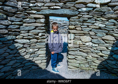 Boy stands à l'entrée d'un clochan à Caher Conor dans péninsule de Dingle, Irlande Banque D'Images