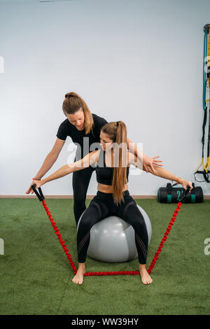 Portrait of a Girl physiothérapeute aide un patient de sexe féminin dans un exercice d'étirement avec une corde rouge sur une balle de caoutchouc. Concept de la santé musculaire et re Banque D'Images