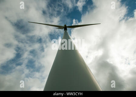 Vue en ligne droite du mât et des pales de l'éolienne vus contre des nuages plus sombres dans un ciel bleu Banque D'Images