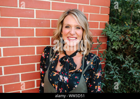 Happy smiling woman in front of brick wall sur journée ensoleillée en Californie Banque D'Images