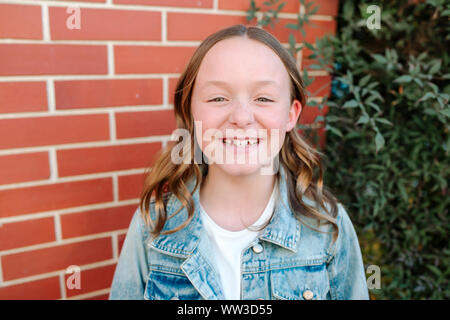 Heureux preteen girl wearing denim jacket par brick wall Banque D'Images
