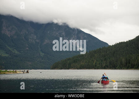 Homme et enfant une Pagaie canoë rouge sur un lac de montagne sur un jour nuageux Banque D'Images