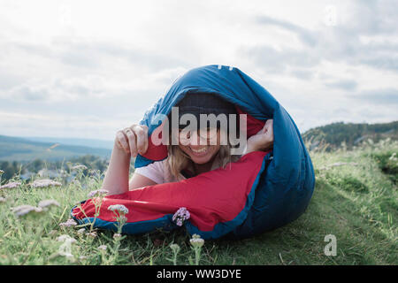 Portrait d'une femme en riant dans un sac de couchage tout en camping à hill Banque D'Images