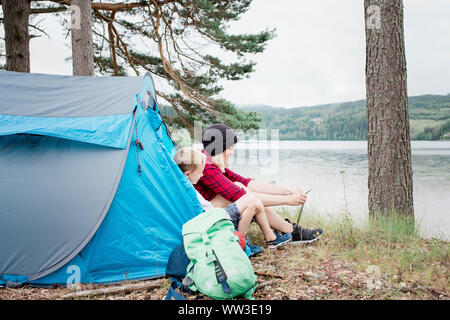 Mère & fils assis dans une tente de camping tout en souriant lacets de liage Banque D'Images