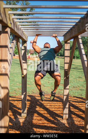 Vue de face d'un homme fort à l'échelle oscillante monkey bars in park Banque D'Images