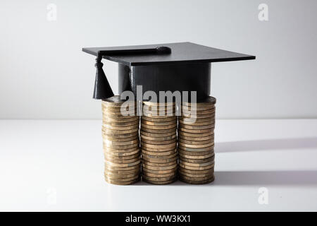 Graduation Cap noir avec pompon près de pièces empilées au fil isolé sur fond blanc Banque D'Images