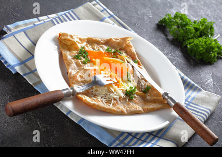 Crêpe bretonne galettes de sarrasin, de la sarriette Bretons avec oeuf renversé, de fromage, de jambon sur une assiette blanche sur une table, close-up Banque D'Images