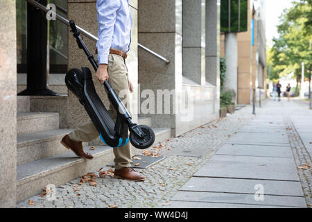 Homme portant l'E-scooter de travailler à la sortie de l'immeuble de bureaux Banque D'Images