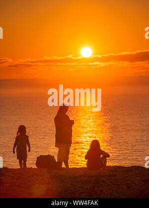 Mère de deux jeunes filles de regarder le coucher du soleil sur la mer à Hoburgen, Gotland, Suède, Scandinavie Banque D'Images