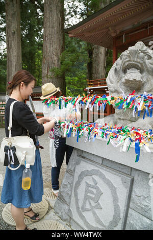 Nikko, Japon. Deux jeunes femmes visiteurs leur attacher du ruban de prière autour de la statue de lion Futarasan shrine annonce à posséder de match-making power. Banque D'Images