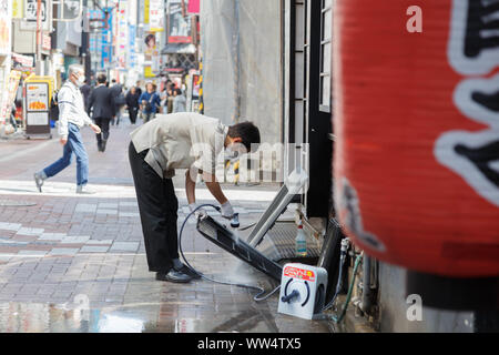 Shinjuku, Tokyo, Japon. Restaurant d'un jeune homme en uniforme travailleur nettoie les pièces de climatiseur à l'extérieur, sur la rue devant la boutique s'ouvre. Banque D'Images