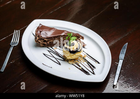 Balle jaune crème glace au chocolat avec garniture et tranche de gâteau au chocolat. Formant un dessert gastronomique. Banque D'Images