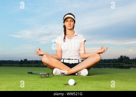 Golfeur fille assis en posture de yoga sur le parcours de golf. Banque D'Images