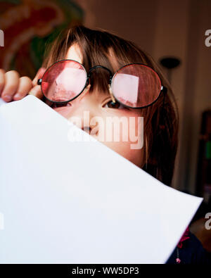 Enfant de 4 ans avec des lunettes, feuille blanche devant la bouche Banque D'Images