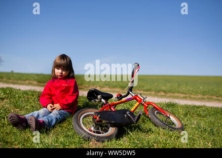5-year-old girl, assis près de la route vélo rouge Banque D'Images