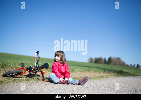 5-year-old girl, assis près de la route vélo rouge Banque D'Images
