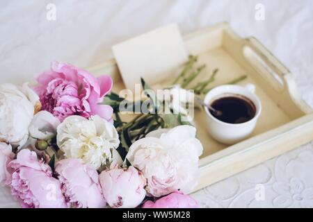 Bouquet de pivoines et d'une tasse de café avec une enveloppe sur un plateau sur un lit Banque D'Images