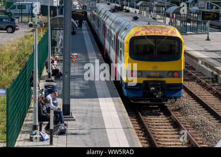 Les personnes en attente sur une plate-forme à l'Etterbeen gare dans le sud de Bruxelles, Belgique, avec un train de banlieue visible Banque D'Images