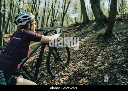 Photo de femme athlète en vélo pour augmenter le port du casque dans la colline de la forêt Banque D'Images