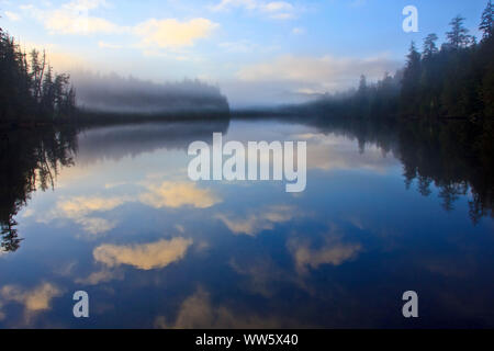 Dans le lac, légèrement bordée d'un paysage montagneux avec le brouillard, dans le lac lisse le ciel avec nuages reflétés, Cape Scott Provincial Park, British Columbia, Canada Banque D'Images