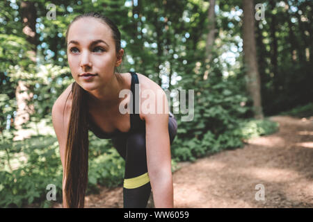 Femme sportive se prépare à exécuter dans la forêt. Jeune athlète femme à l'avant en position de départ pour la course. Portrait d'un certain jogger est Banque D'Images