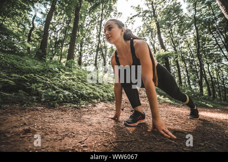 Low angle view of a sports confident female se prépare à exécuter dans la forêt. Jeune athlète femme à l'avant et prêt pour la course. Banque D'Images