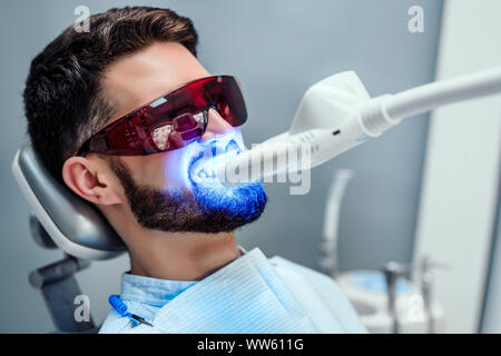 Vue rapprochée de l'homme subissant un traitement de blanchiment des dents au laser pour enlever les taches et la décoloration. Banque D'Images