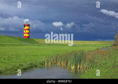 Voir ci-dessus un fossé couvert de roseaux sur le phare de Pilsum la Frise orientale Krummhoern en face de nuages de pluie. Banque D'Images