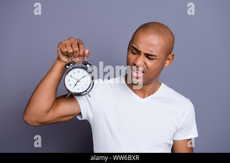 La photo en gros malade masculin malsain peau noire il lui sa tête chauve macho perplexe tenir réveil acier horreur d'aller travailler au début dégoûté wearing white t Banque D'Images