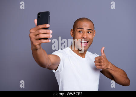 La photo en gros plan de la peau sombre sain il lui sa coiffure courte macho thumb up faire prendre des autoportraits excité appel vidéo heureux bouche ouverte portant des T-shirt blanc Banque D'Images