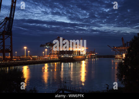 Hambourg, août 2013 : porte-conteneurs / Freighter au crépuscule / Nuit (heure magique) dans le port de Hambourg avec de grands portiques à conteneurs (Arc Banque D'Images