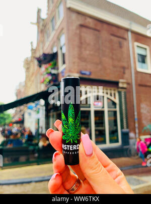 Amsterdam / Pays-Bas - 11 juillet 2019 : Noir plus léger en main avec l'icône féminine de la marijuana sur fond d'un café dans le centre d'Amsterdam. Banque D'Images