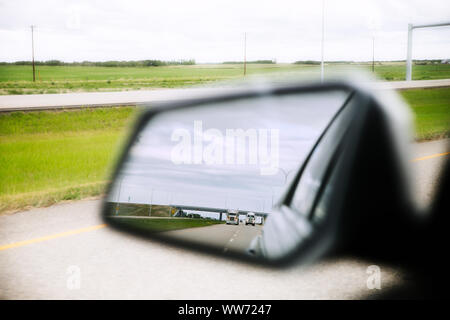 Close up d'un rétroviseur latéral avec deux gros camions semi reflétée dans le miroir le long d'une autoroute dans un paysage rural landscape Banque D'Images