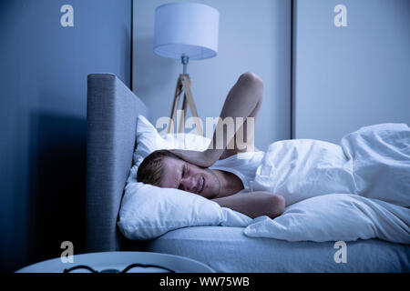 L'homme qui couvre sa tête avec oreiller au lit Banque D'Images