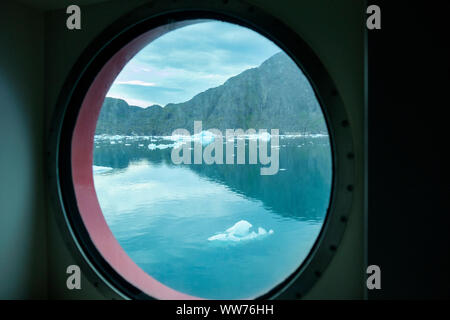 Petits icebergs et des falaises rocheuses vue à travers un hublot du navire de croisière fjord à partir de la fenêtre dans Bredefjord à Narsaq Kujalleq, Groenland, Banque D'Images