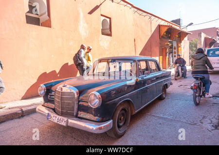 Vieille voiture et passant sur le vélo Petite rue de la médina de Marrakech de la vieille ville. À Marrakech les maisons sont traditionnellement rose. Le Maroc. Banque D'Images