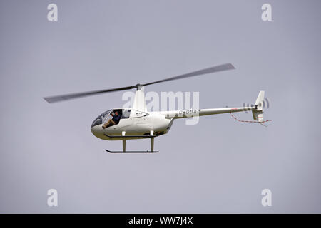 Photographe assis à la porte ouverte de Robinson R44 G-L'OCAF Hélicoptère léger photograping au Le RIAT Banque D'Images