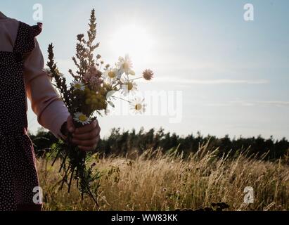 Les jeunes filles main tenant des fleurs sauvages dans une prairie au coucher du soleil Banque D'Images