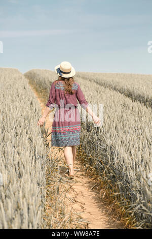 Jeune femme en robe d'été et avec chapeau de paille sur le champ de grain Banque D'Images