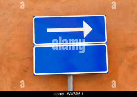 XWOne way directional arrow sign blanc avec un panneau additionnel vide contre un mur rouge. Banque D'Images