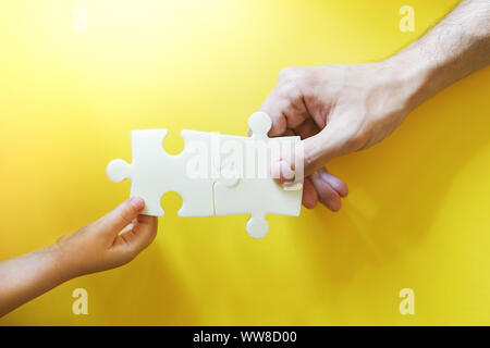 Père de l'enfant et en tenant les mains des morceaux de puzzle. Concept de famille joyeuse et amicale. Backrgound jaune vif. Banque D'Images