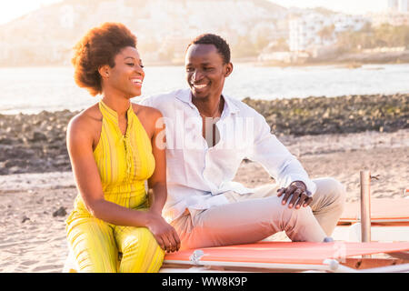 Happy black race african couple sur la plage de sourire et de profiter de l'activité de loisirs ensemble assis près de la côte de l'océan l'heure d'été et aime vibes pour les jeunes en locations Banque D'Images