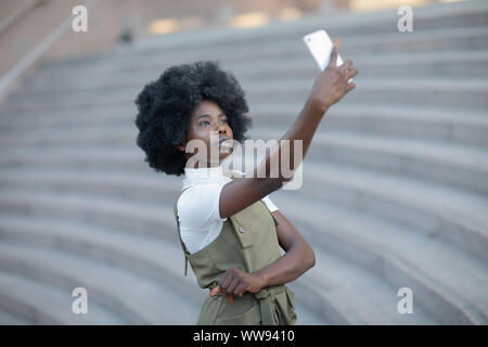 Attractive african american woman de prendre une photo d'elle-même avec son téléphone portable sur un escalier amphithéâtre Banque D'Images