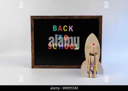 Tableau noir avec texte retour à l'école avec des fusées et des crayons de couleur sur fond blanc Banque D'Images