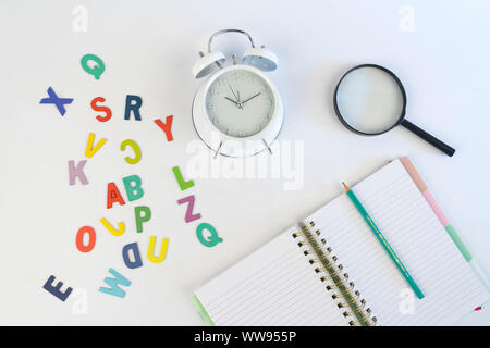 Réveil, ordinateur portable, lettres de couleur et une loupe sur fond blanc. Vue de dessus Banque D'Images