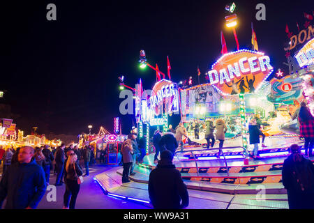 Les adolescents regarder les voitures sur une roue tournante fairground ride zip passé à une période nocturne de foire dans Hambourg, Allemagne Banque D'Images