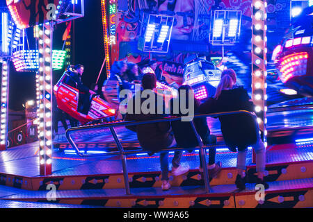 Les adolescents regarder les voitures sur une roue tournante fairground ride zip passé à une période nocturne de foire dans Hambourg, Allemagne Banque D'Images