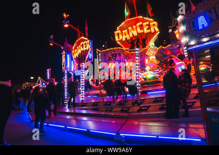 Les adolescents regarder les voitures sur une roue tournante fairground ride zip passé à une période nocturne de foire dans Hambourg, Allemagne Banque D'Images